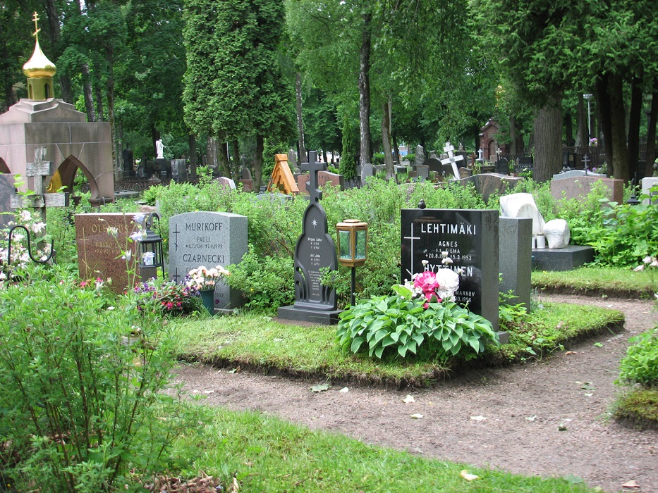 Ortodoksiristi hautausmaalla hautakivien ja puuristien joukossa.